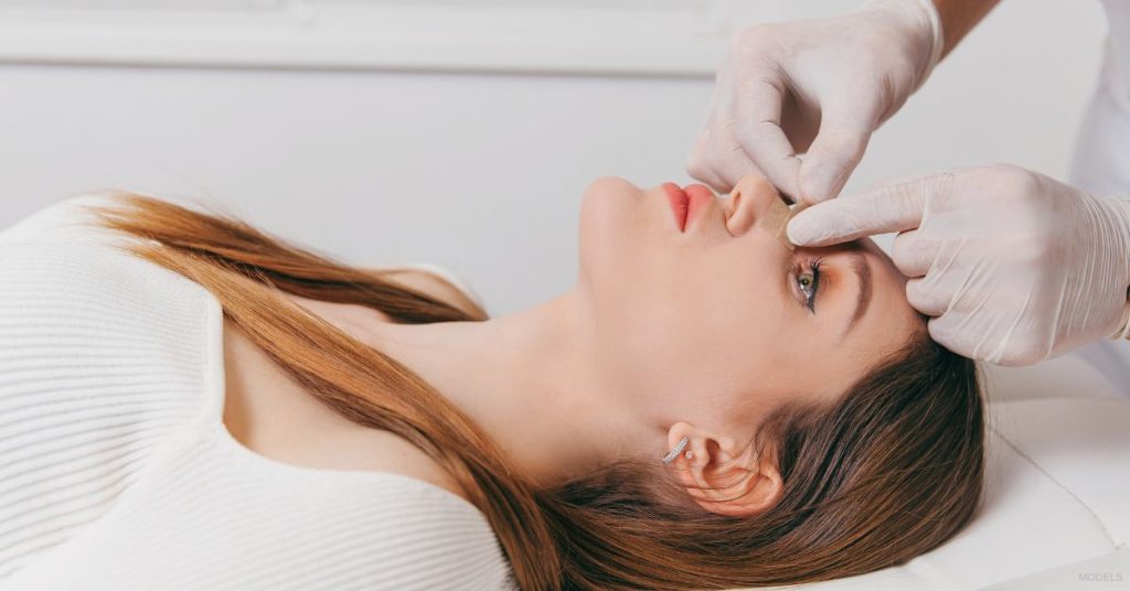 Doctor examining patient's nose (MODELS) after rhinoplasty.